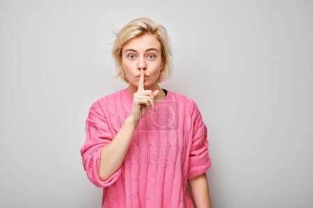 Photo for Portrait of woman making a shushing gesture with her finger on lips, against a gray background. - Royalty Free Image