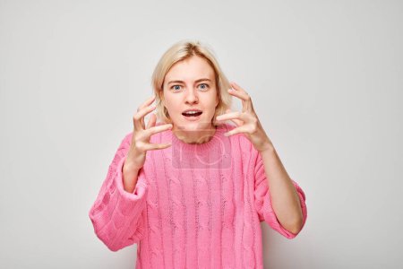 Surprised young woman in pink sweater gesturing with hands, isolated on white background.