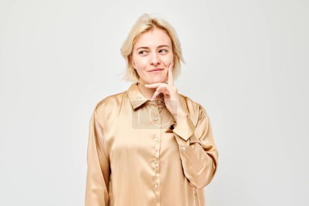 Téléchargez les photos : Femme confiante dans un chemisier satiné souriant avec une main sur le menton sur un fond clair. - en image libre de droit