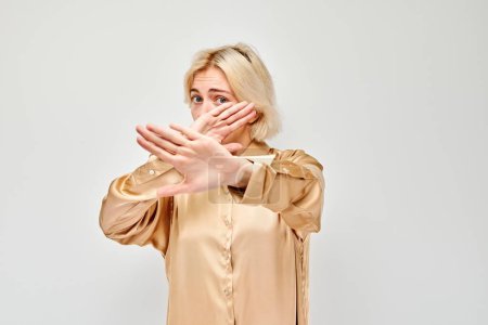Téléchargez les photos : Femme blonde faisant un geste d'arrêt les mains croisées, signalant des frontières ou un déni, fond clair - en image libre de droit
