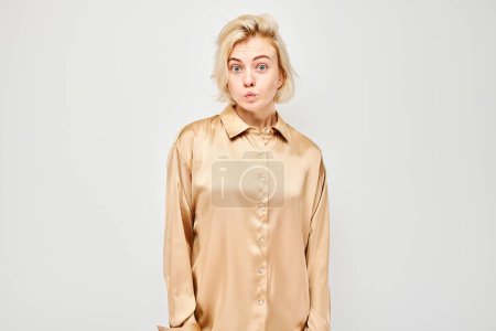 Téléchargez les photos : Jeune femme confus dans un chemisier beige, faisant une expression perplexe sur un fond gris clair. - en image libre de droit