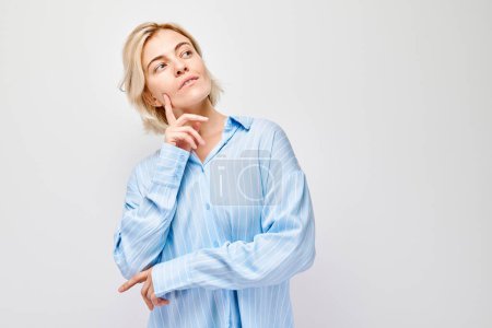 Photo for Woman in blue shirt pondering with hand on chin, isolated on light background. - Royalty Free Image