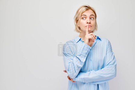 Téléchargez les photos : Femme réfléchie avec un doigt sur le menton, regardant ailleurs, isolée sur un fond clair. - en image libre de droit