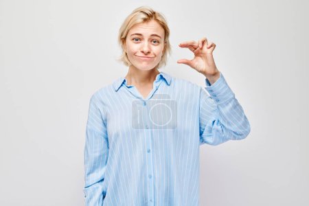 Téléchargez les photos : Femme souriante en chemise bleue faisant un petit geste avec ses doigts, isolée sur un fond clair - en image libre de droit