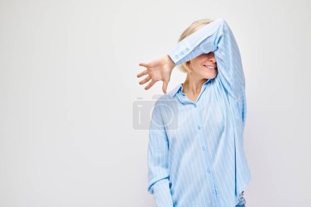 Téléchargez les photos : Femme en chemise bleue couvrant le visage avec le bras, fond blanc. - en image libre de droit