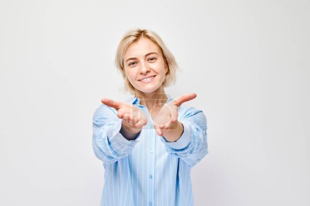 Smiling woman in blue shirt offering hands forward on a white background.