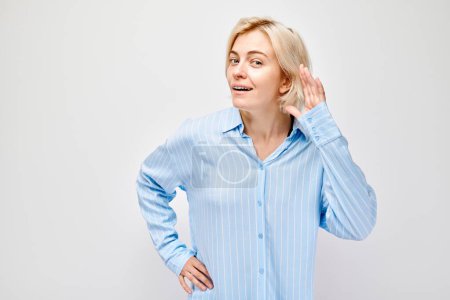 Téléchargez les photos : Femme en chemise bleue écoutant avec la main à l'oreille, fond blanc. - en image libre de droit