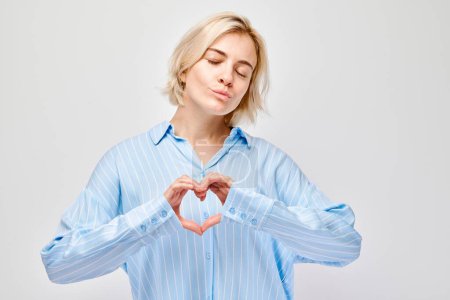 Photo for Woman in blue shirt making heart shape with hands, eyes closed, expressing love and happiness. - Royalty Free Image