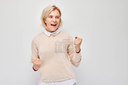 Téléchargez les photos : Portrait de visage souriant jeune femme blonde serrant les poings et se réjouissant, célébrant la victoire isolée sur fond de studio blanc, banne publicitaire - en image libre de droit