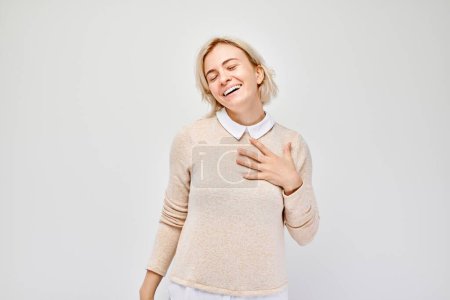 Joyful woman laughing with closed eyes, hand on chest, against a white background.