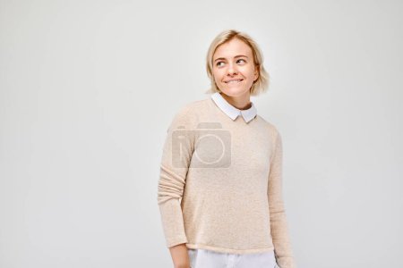 Photo for Smiling woman in casual attire looking away against a plain background, expressing positivity and contentment. - Royalty Free Image
