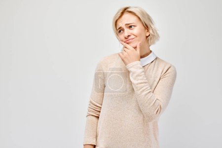 Photo for Thoughtful woman with a subtle smile, hand on chin, looking away on a plain background. - Royalty Free Image