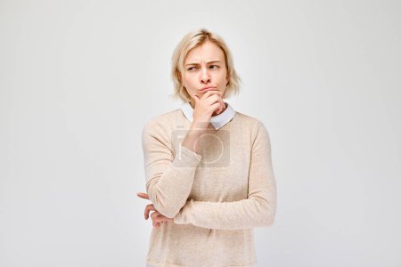 Foto de Mujer meditando con la mano sobre la barbilla, mirando hacia otro lado, sobre un fondo gris claro. - Imagen libre de derechos