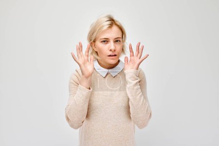 Téléchargez les photos : Femme en pull beige regardant surpris avec les mains en l'air, isolé sur fond blanc. - en image libre de droit