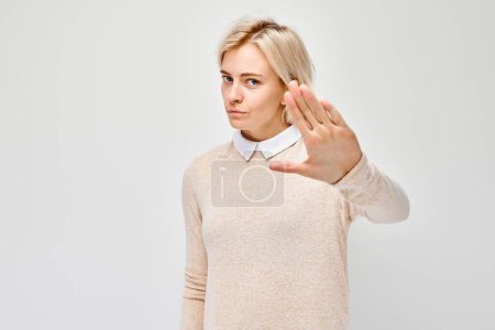 Foto de Mujer rubia mostrando gesto de stop con la mano, sobre un fondo claro. - Imagen libre de derechos