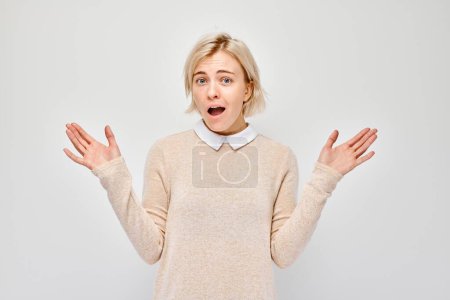 Photo for Surprised young woman with open mouth and raised hands, expressing shock and disbelief, isolated on a light background. - Royalty Free Image