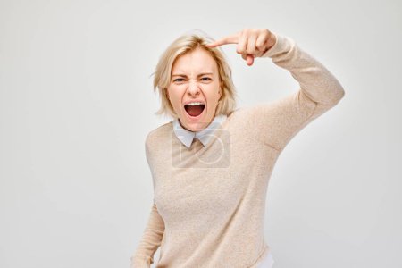 Téléchargez les photos : Portrait de femme blonde en colère pointe son doigt vers la caméra et crie sur fond blanc - en image libre de droit