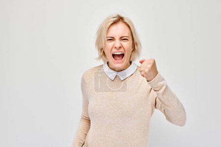 Foto de Retrato de una rubia enojada apretando los puños y gritando sobre un fondo blanco - Imagen libre de derechos