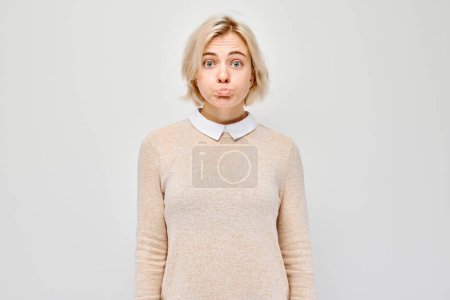 Téléchargez les photos : Jeune femme surprise avec une expression drôle, debout sur un fond gris clair. - en image libre de droit
