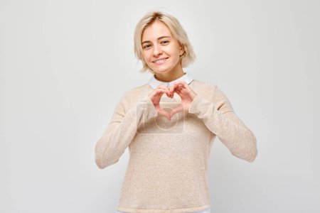 Téléchargez les photos : Femme souriante en forme de cœur avec les mains, isolée sur fond blanc - en image libre de droit