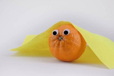Photo for Funny picture, orange fruit with toy eyes under a yellow blanket - Royalty Free Image