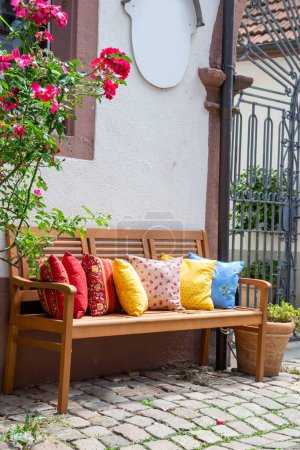 Wood romantic bench with a lot of multicolor pillows outdoor near stone house and rose.
