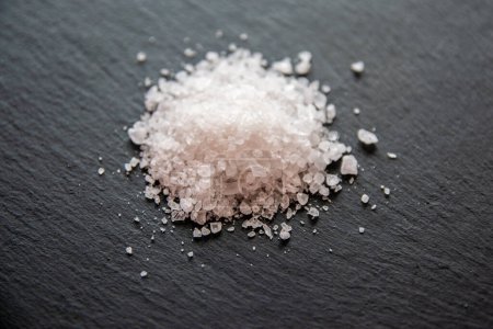 Montón de sal marina sobre un fondo negro natural. Cristales de sal blanca para cocinar alimentos.