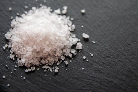 Cristales de sal para cocinar la comida. Montón de sal marina sobre un fondo negro natural. 