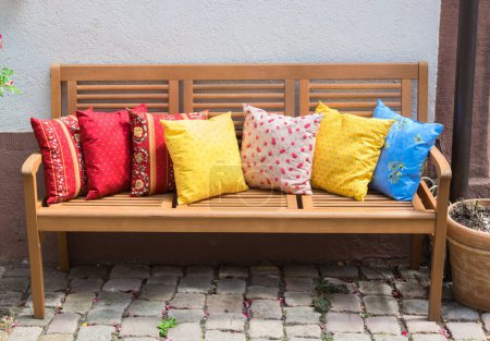 Wood romantic bench with a lot of multicolor pillows outdoor near stone house.