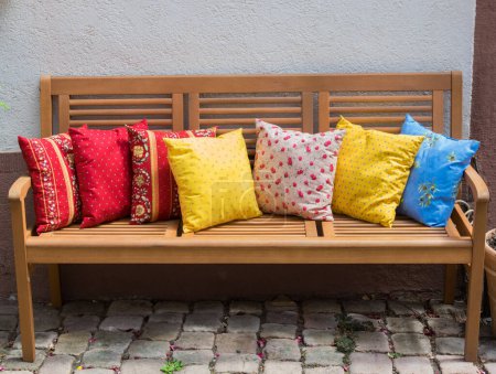 Wood romantic bench with a lot of colorful pillows outdoor near stone house in summer day.