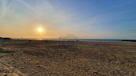 Grande plage de sable près de la mer avec maisons et hôtel. Un peuple marchant sur la plage du coucher du soleil dans la soirée.