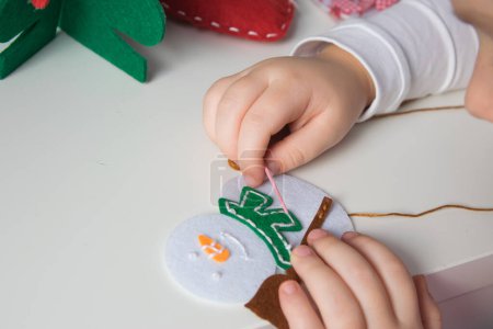 Die Hand des Kindes machen Schneemann und Weihnachtsbaum mit Nadel, Faden für Weihnachtsgrußkarte. Hobby Konzept. Handgefertigt.