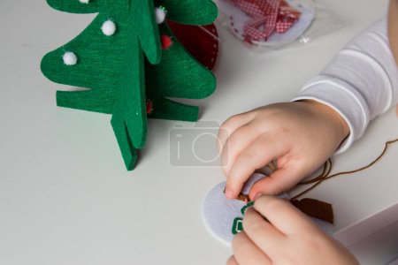 The hand of the child make snowman and christmas tree with needle, thread for christmas greeting card. Hobby concept. Handmade.