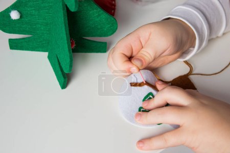 La main de l'enfant faire bonhomme de neige et arbre de Noël avec aiguille, fil pour carte de voeux de Noël. Concept de passe-temps. Fait à la main.