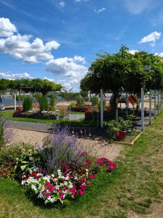 Schöner Garten mit vielen Blumen und Bäumen in Flussnähe an sonnigen Sommertagen.
