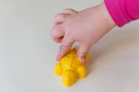 Hände des Kindes, die das kleine Spielzeug auf dem Holzgrund halten. Gelbe Plastikschildkröte in den Kinderhänden. 