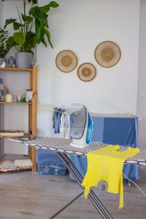 Una plancha azul en la tabla de planchar con una ropa de bebé amarilla