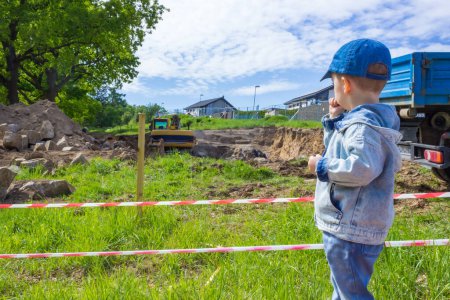 A boy looks at the construction of a housing complex, clearing rocks with a skid steer tractor. High quality photo