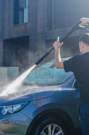 El hombre lava su auto afuera. El conductor utiliza un equipo de lavado especial profesional para lavar la carrocería del automóvil. Foto de alta calidad.