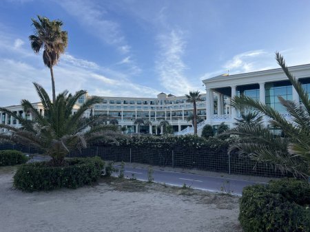Cette image met en valeur un hôtel luxueux en bord de mer niché parmi de grands palmiers tropicaux oscillants dans le contexte d'un ciel sombre. L'architecture élégante des hôtels est complétée par la verdure luxuriante