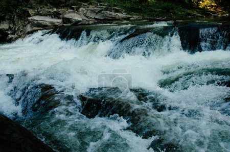 Eine wunderschöne Aussicht auf Wasser, das auf dem Weg den Berg hinunter mit hoher Geschwindigkeit über felsige Wasserfälle fließt. Hochwertiges Foto