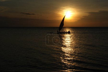 Silhouette eines Fischerbootes mit ausgestreckten Segeln. Hintergrund Sonnenuntergang. Der Himmel ist orange