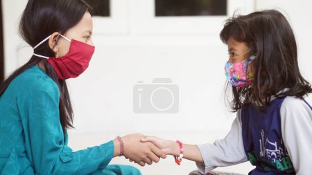 Two girls wearing masks shake hands