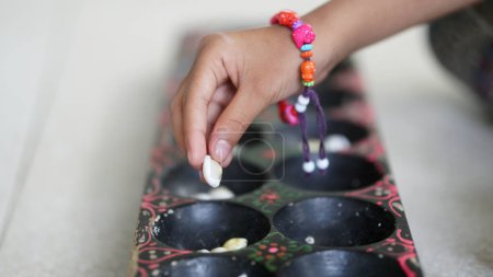 A girl's hand is playing Dakon, a traditional Indonesian children's game