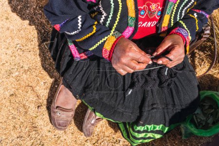 les mains d'une femme andine filant de la fibre d'alpaga brune dans un rouet ancestral de la chaîne des Andes dans un atelier artisanal éclairé par la lumière naturelle