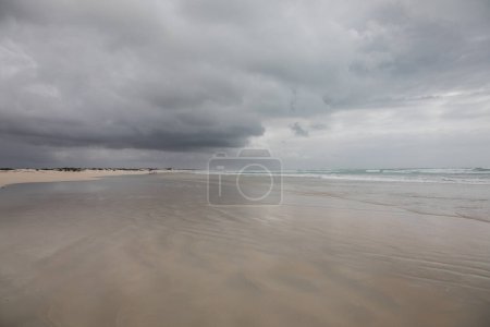 Dramatic cloud sky reflecting in the water washing up on a deserted beach