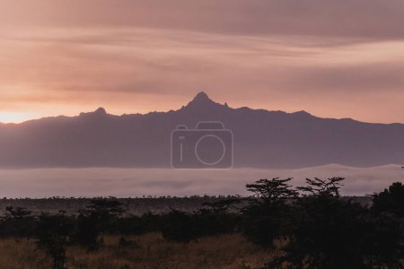 Fiery sunset silhouettes Mount Kenya over misty landscape