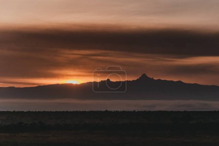Fiery sunset silhouettes Mount Kenya over misty landscape