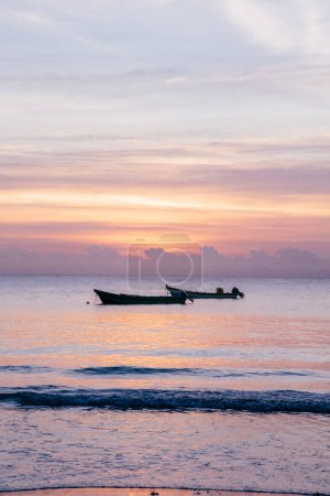 Serene sunset over calm sea with anchored boats in Tulum