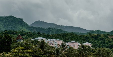Bâtiments colorés à flanc de colline nichés dans une verdure luxuriante sur fond de montagne brumeuse en Martinique.